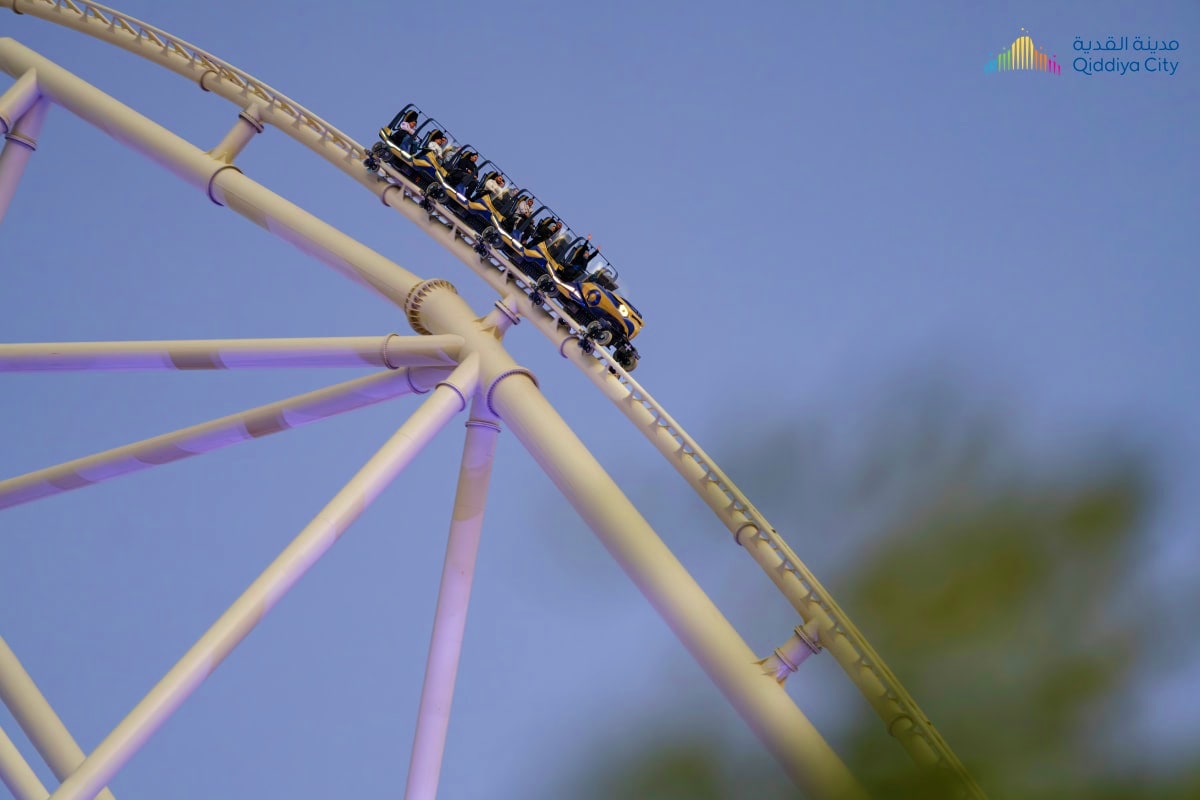 Roller coaster train climbing steep track at Qiddiya City amusement park in Riyadh against clear blue sky