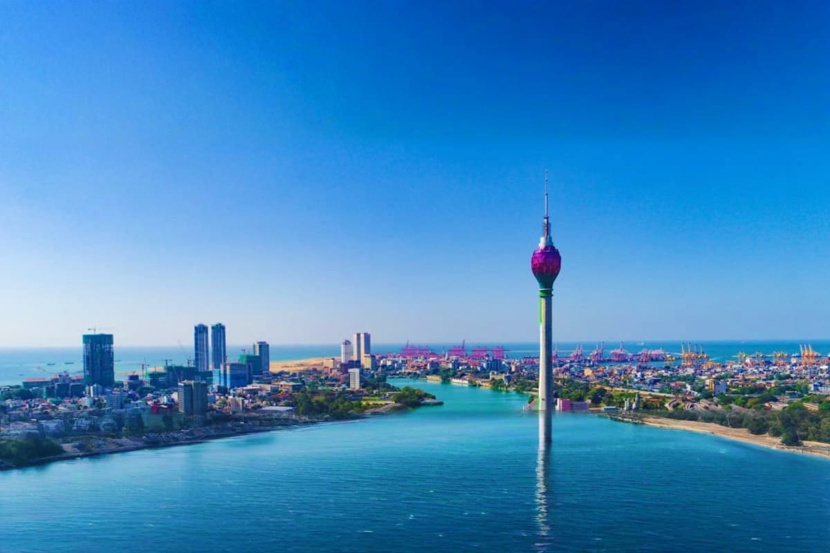 Aerial view of Colombo skyline with modern tower, turquoise harbor waters, and coastal cityscape under clear blue sky
