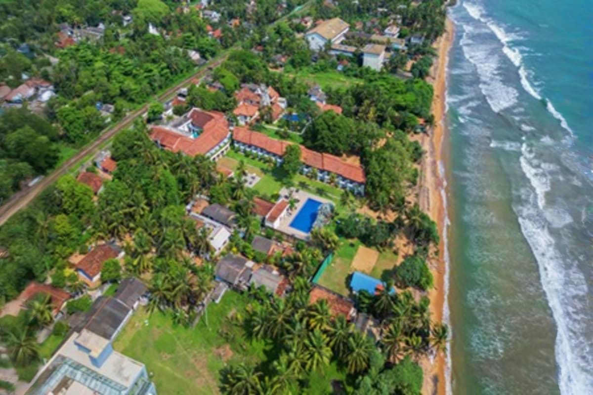 Aerial view of beachfront residential area in Sri Lanka with turquoise ocean, white sand beach, and lush tropical vegetation 