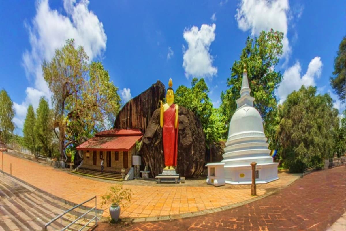 Buddhist temple complex with golden Buddha statue, white stupa, traditional wooden shrine building, and tall trees under blue