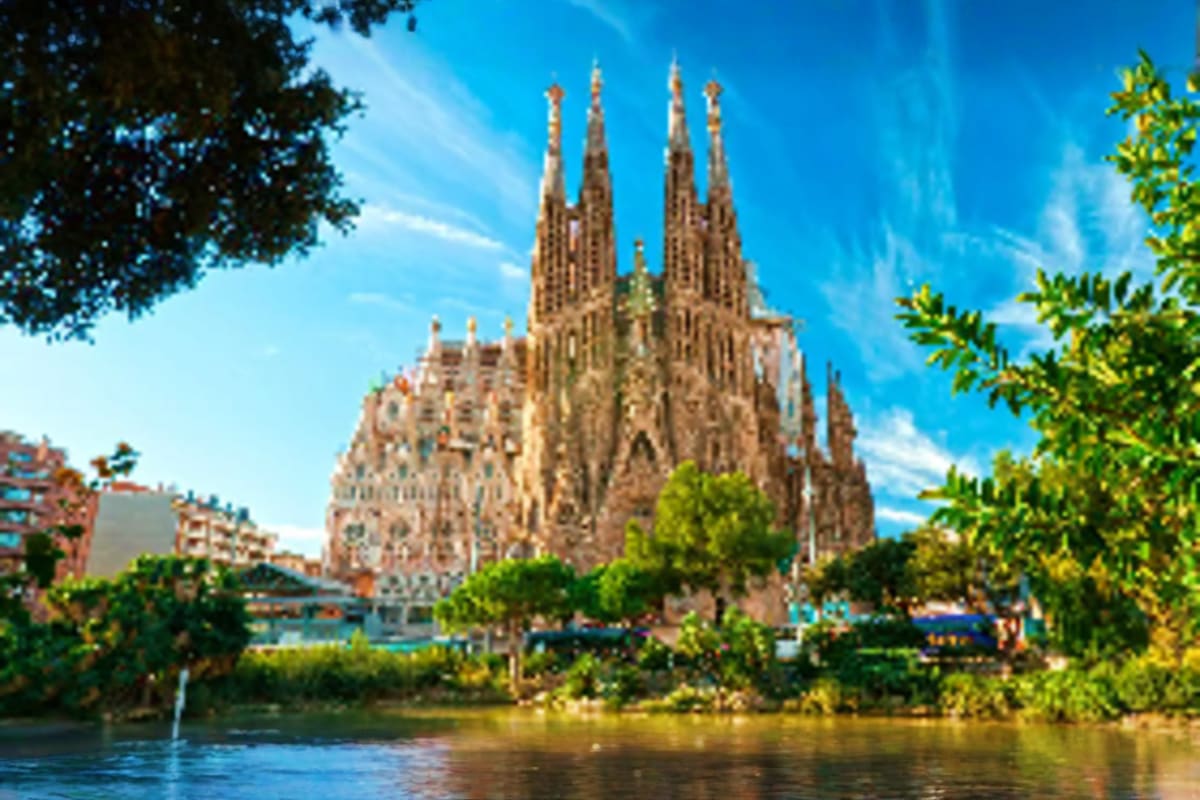 Sagrada Familia basilica viewed from across river with green trees and blue sky in Barcelona, Spain