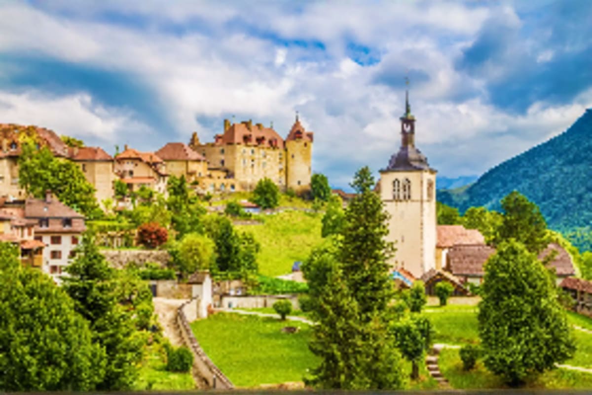 Medieval castle overlooking Alpine village with church spire and lush green mountains in Bavaria, Germany