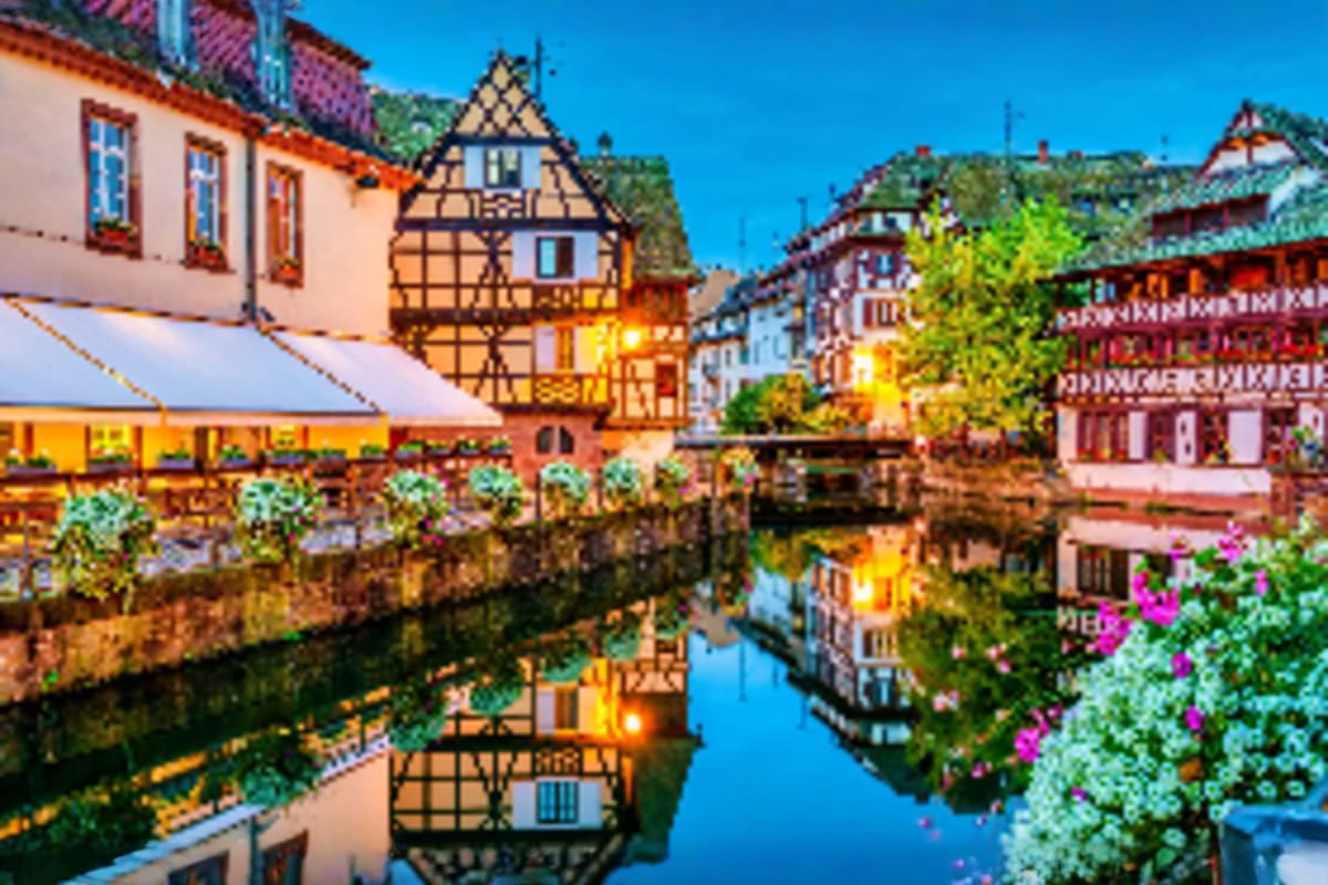 Half-timbered medieval buildings reflecting in a calm canal with colorful flowers and ivy in a charming European town square
