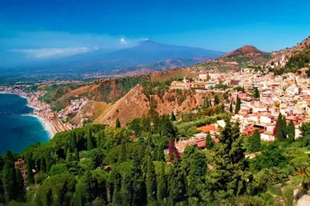 Classical Italy and Switzerland IND Aerial view of Taormina, Sicily with Mediterranean coastline, Mount Etna volcano in distance, and cypress trees dotting hills