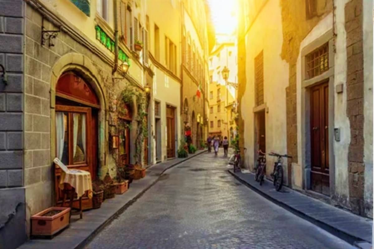 Classical Italy and Switzerland IND Sunny narrow cobblestone street in historic Italian town with yellow buildings, arched doorways, and bicycles parked along th