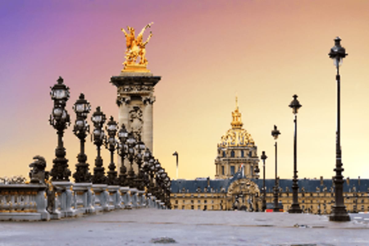 Bridge at Palace of Versailles with ornate lamp posts and golden statues at sunset in Paris, France.