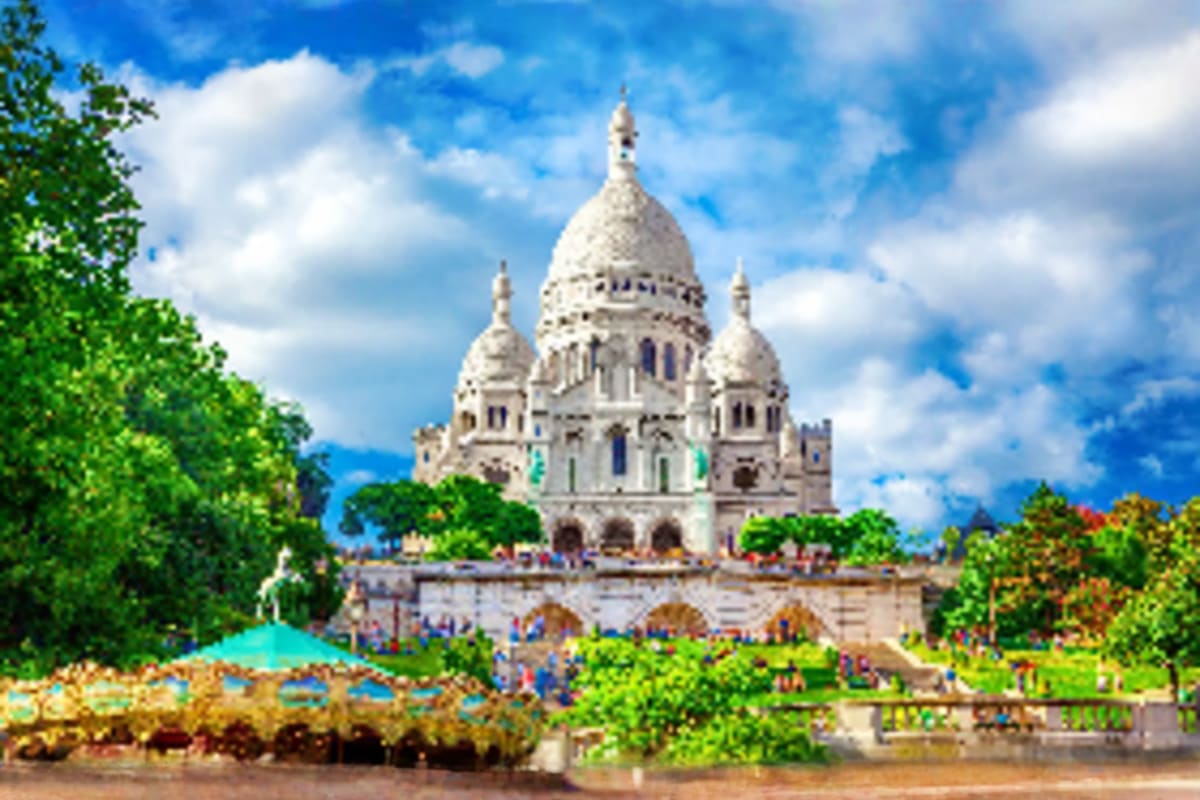 Sacré-Cœur Basilica in Paris with white dome and bell towers, surrounded by green trees and blue sky with clouds