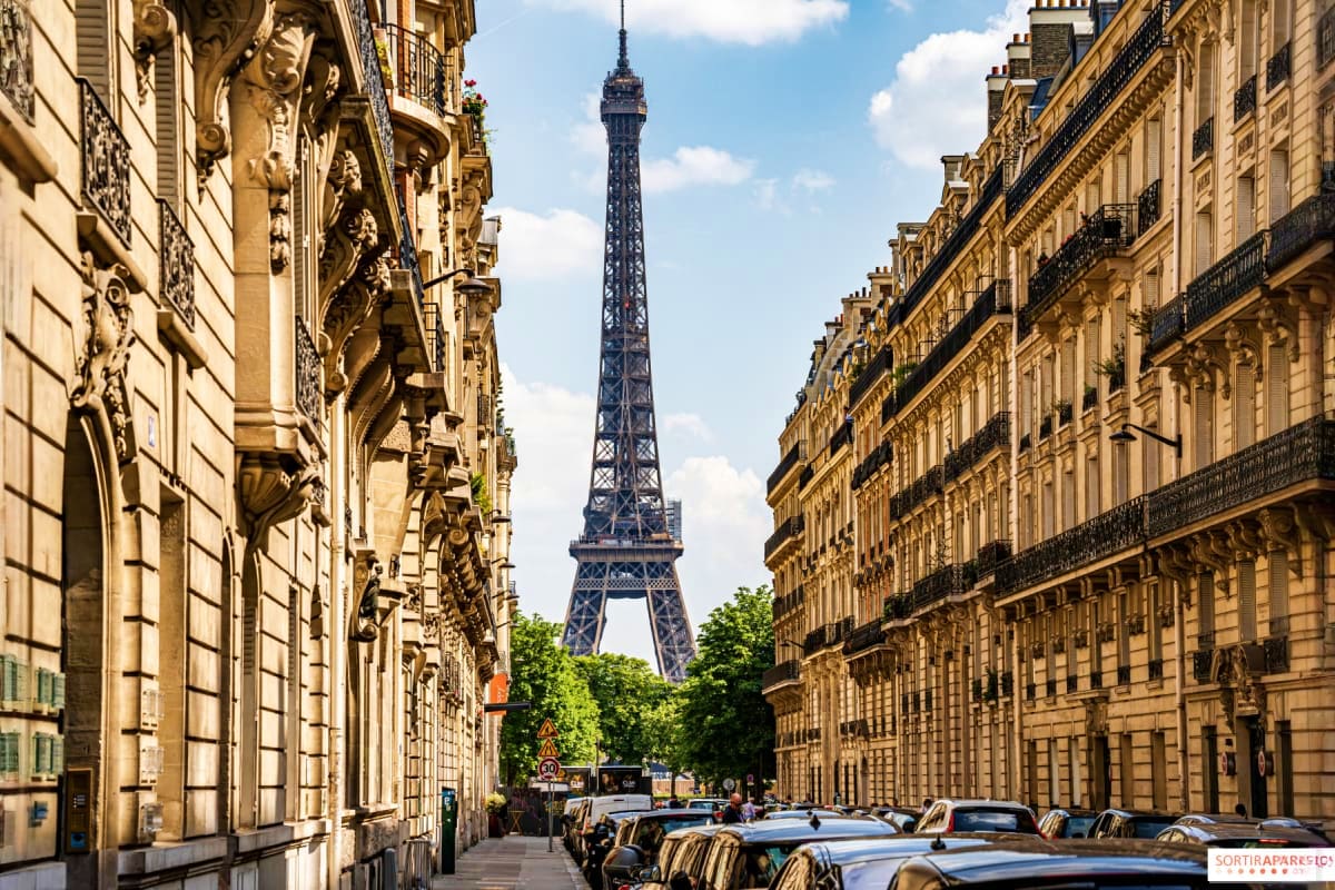 Eiffel Tower viewed down a Parisian street lined with ornate Haussmann buildings and parked cars under blue sky