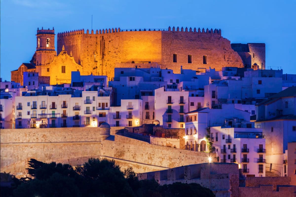 Peñíscola castle illuminated at dusk overlooking white and blue Mediterranean buildings in Spain