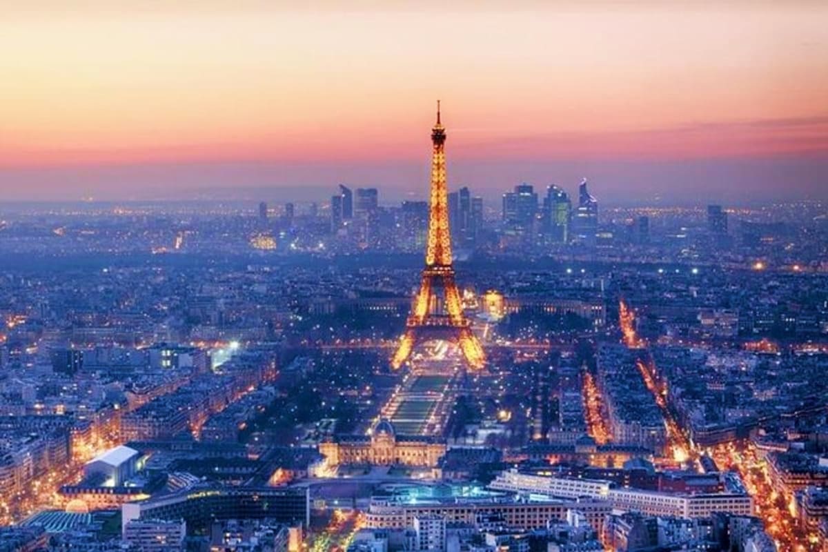 Eiffel Tower illuminated at dusk with Paris cityscape and surrounding buildings lit up at twilight