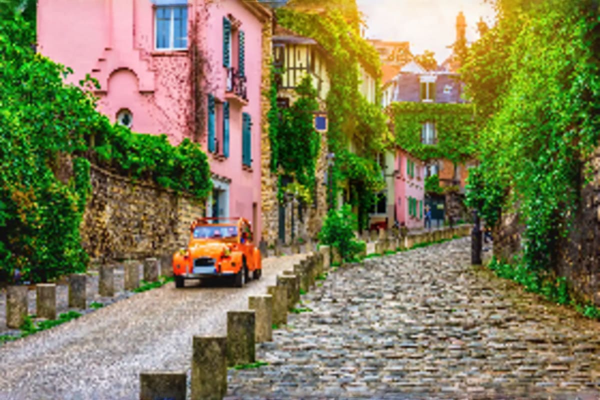 Vintage orange car on a narrow cobblestone street lined with ivy-covered historic buildings in a European village