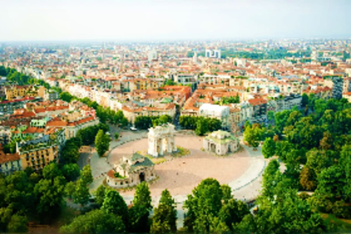 Aerial view of a European city with a historic fortress or citadel in the foreground surrounded by green trees and residentia