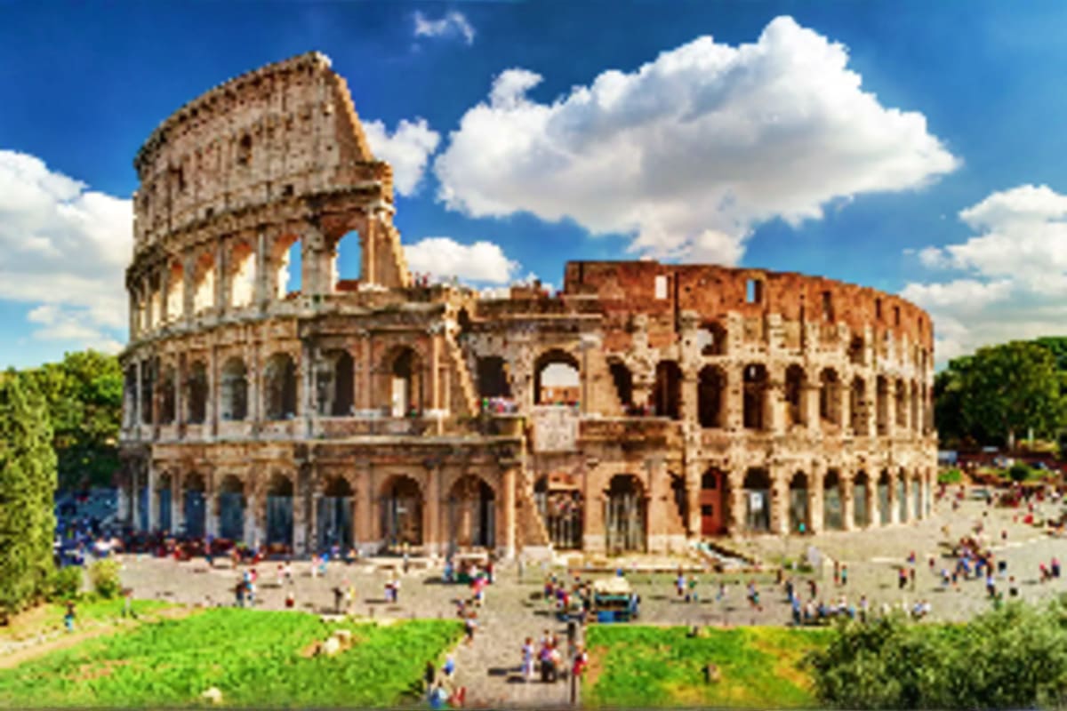 Ancient Roman Colosseum ruins in Rome with tourists gathered in the plaza on a sunny day with blue sky and white clouds