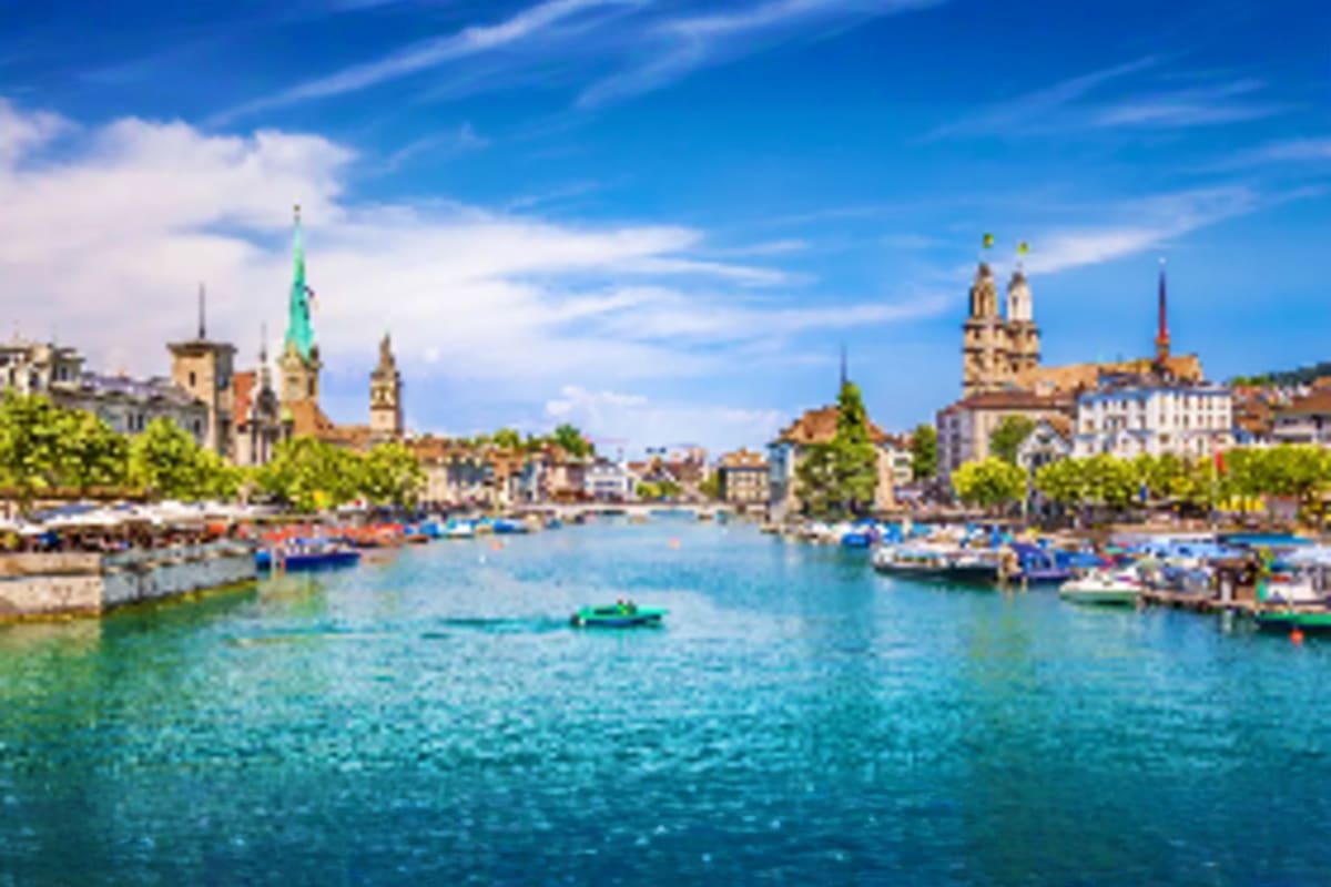 Zurich waterfront with church spires and boats on the Limmat River under blue sky