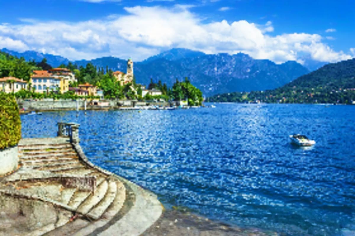 Stone waterfront promenade overlooking alpine lake with mountain village and church tower across the water, surrounded by for