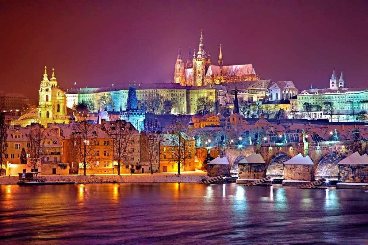 Prague castle and St. Vitus Cathedral illuminated at night with Vltava River and Charles Bridge in foreground