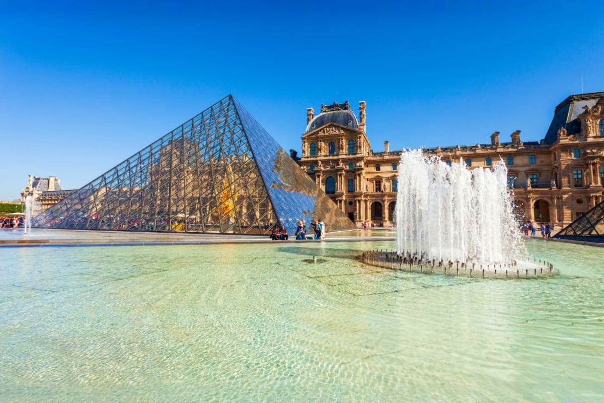 Louvre Museum with glass pyramid entrance, fountain, and historic palace building in Paris courtyard on sunny day
