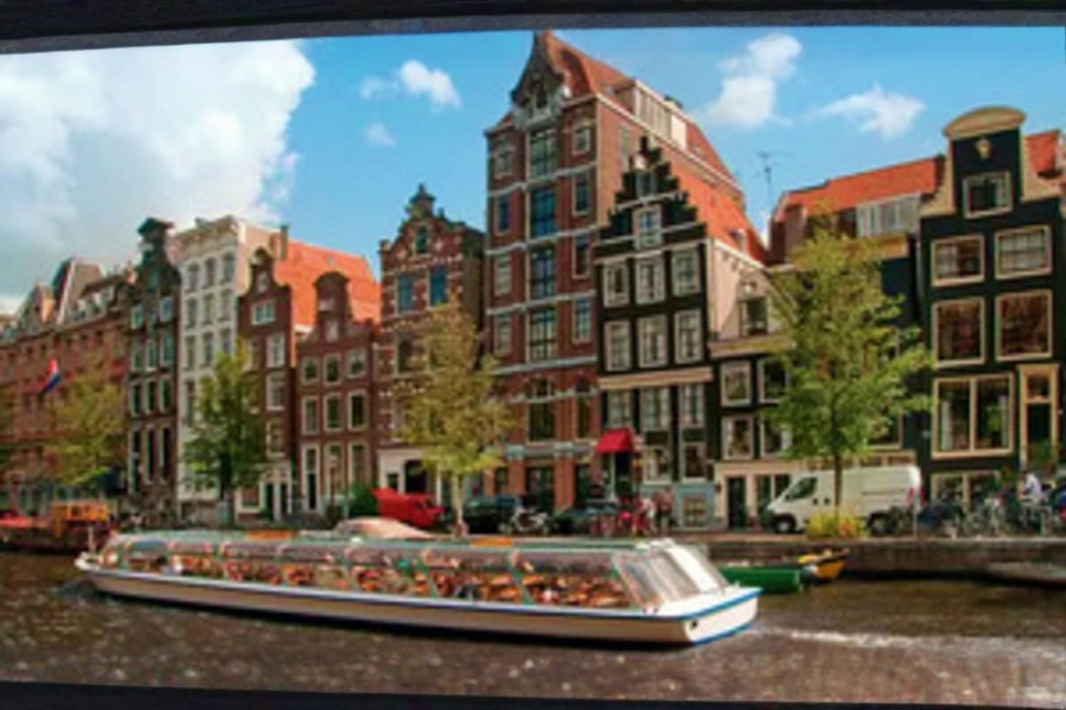 Tour boat with passengers on Amsterdam canal lined with historic Dutch buildings with characteristic gabled roofs