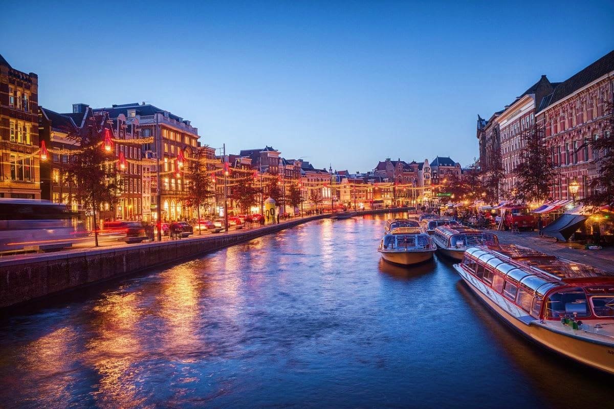 Evening canal view in Amsterdam with illuminated historic buildings and tour boats on the water at dusk