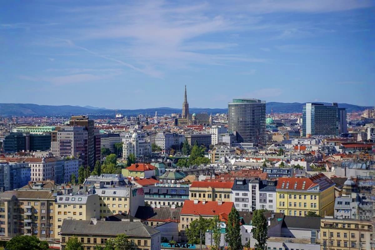 Vienna cityscape with St. Stephen's Cathedral spire in background, residential and modern buildings in foreground, surrounded
