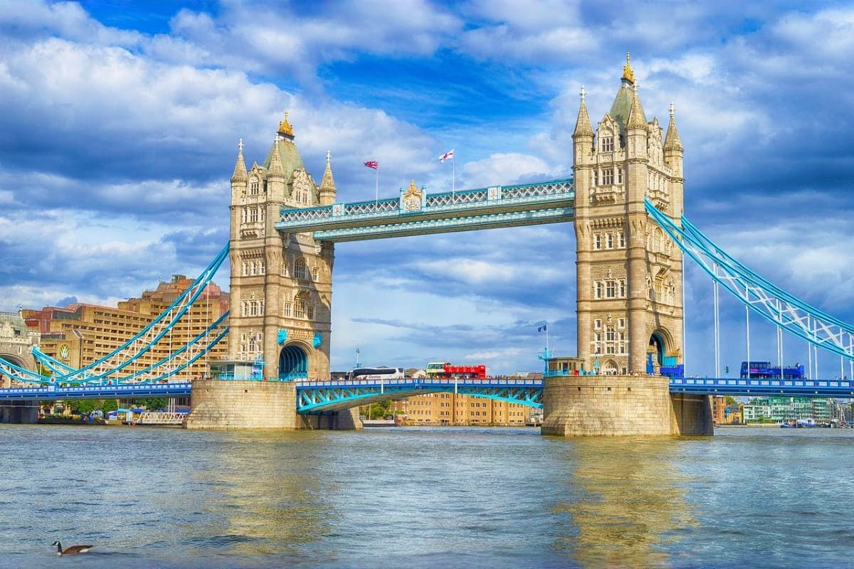 Tower Bridge spanning the River Thames in London with iconic stone towers and blue suspension cables under cloudy sky