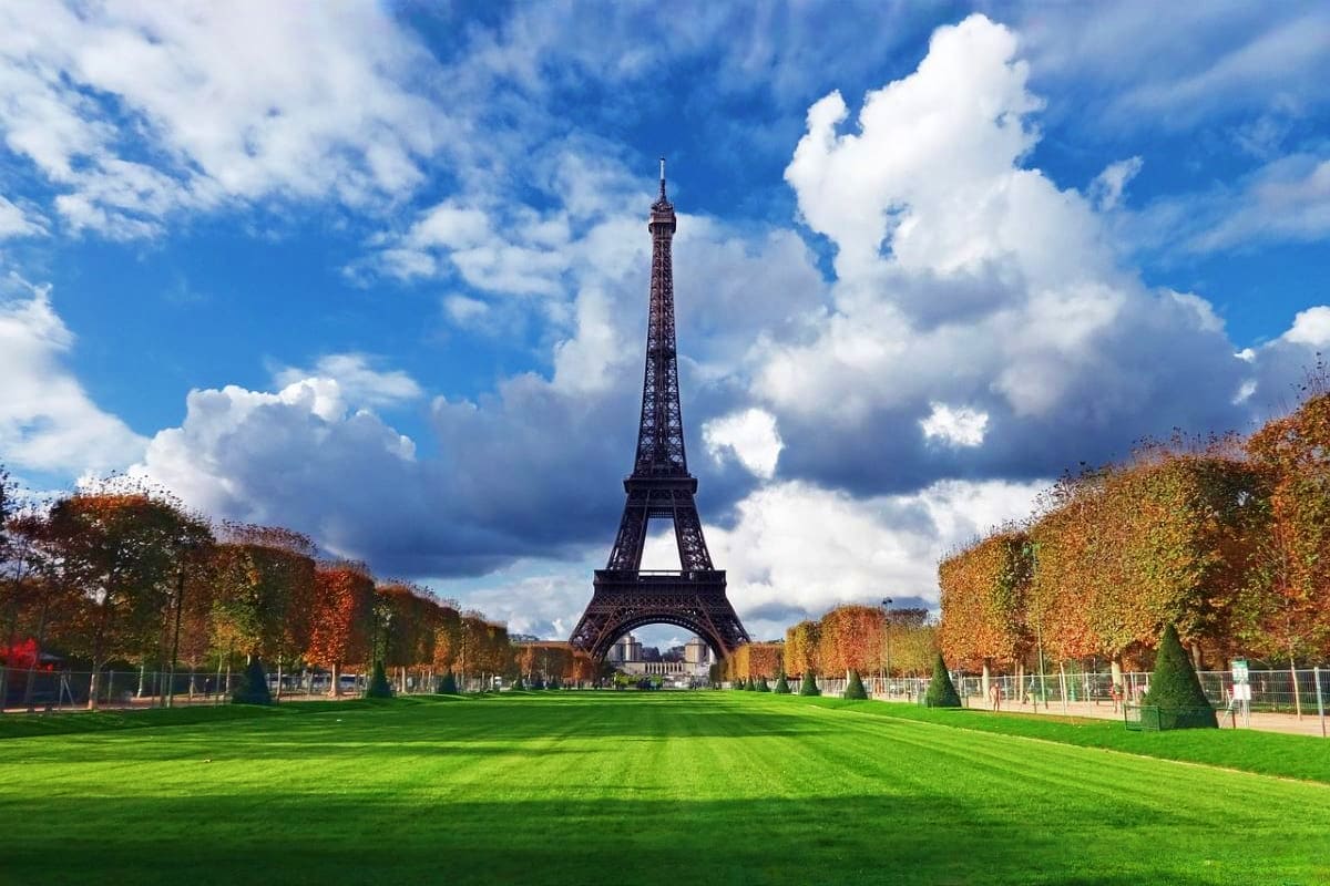 Eiffel Tower viewed from Champ de Mars in Paris with green lawn, autumn trees, and blue cloudy sky