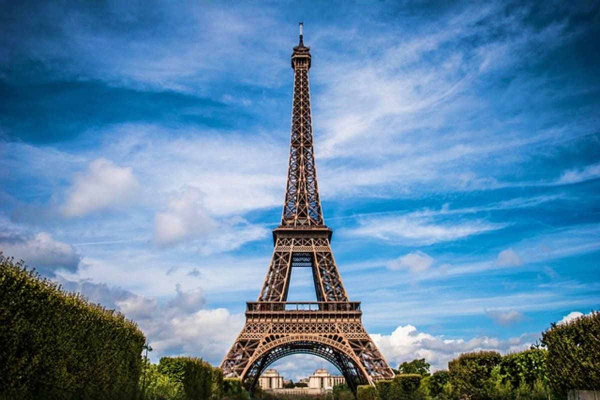 Eiffel Tower in Paris standing tall against a blue sky with green tree-lined boulevards on either side
