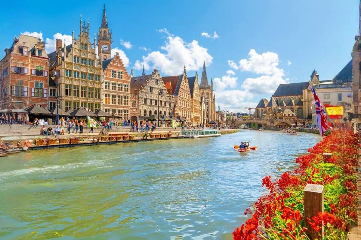 Historic riverside square in Ghent, Belgium with colorful medieval guild houses and church spires overlooking the water canal