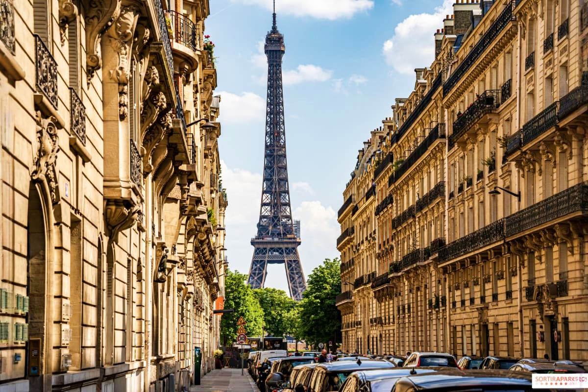 Parisian street lined with ornate Haussmann buildings framing the Eiffel Tower in the distance under blue sky