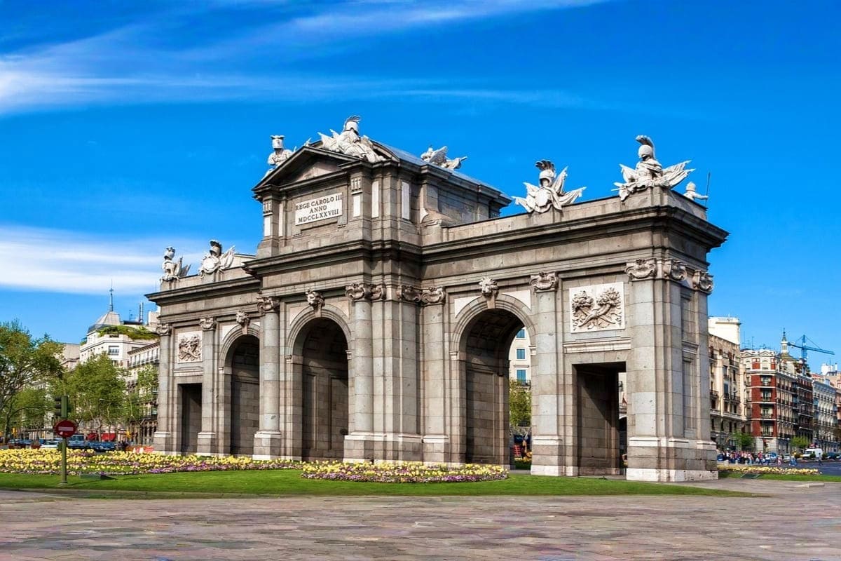 Puerta de Alcalá monument in Madrid with neoclassical architecture, multiple arches, and ornamental sculptures under clear bl