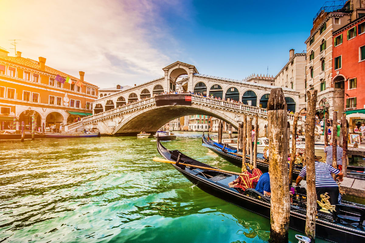 Gondolas moored in Grand Canal with Rialto Bridge and colorful Venetian buildings under blue sky in Venice, Italy