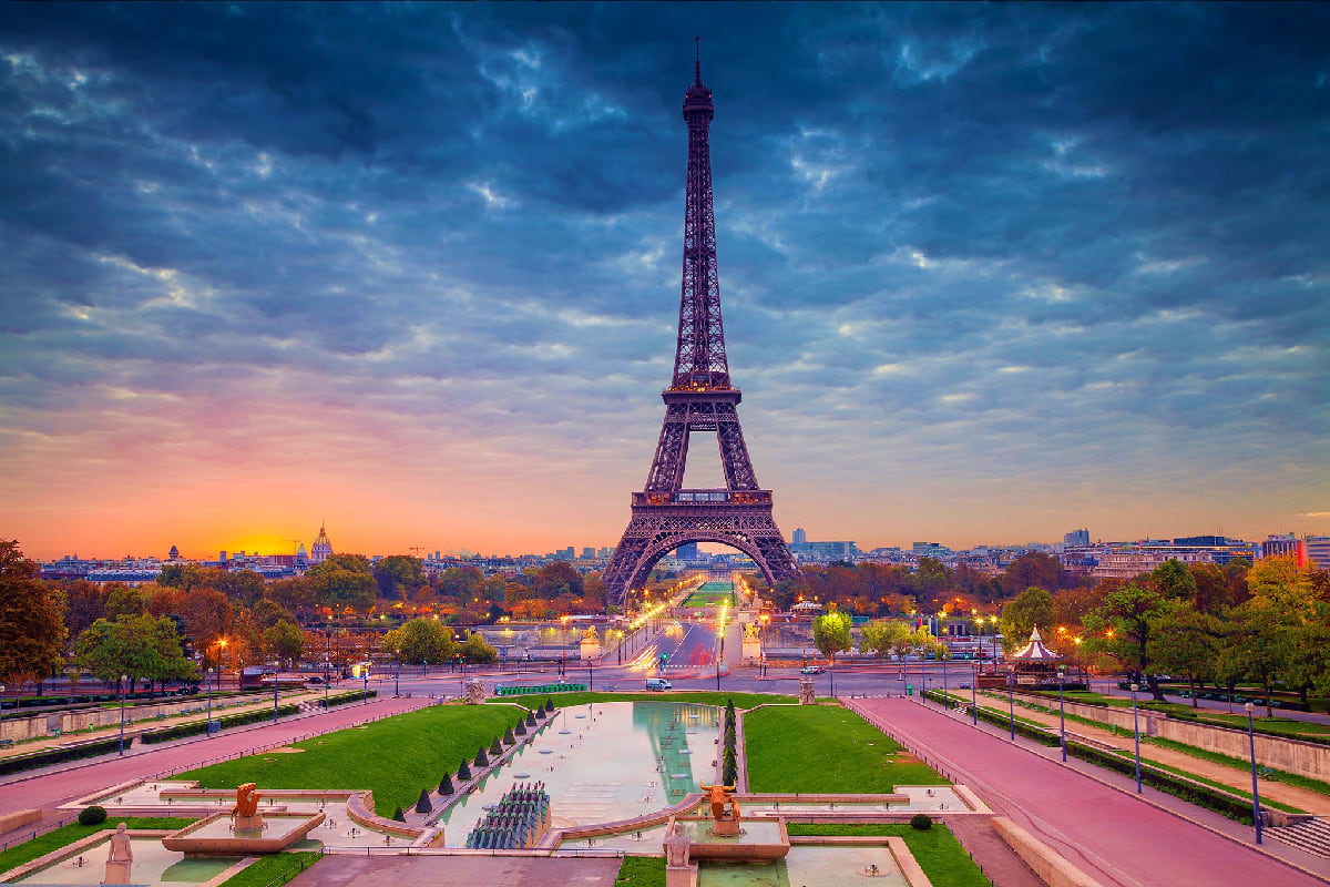 Eiffel Tower at sunset in Paris with Trocadéro Gardens, reflecting pool, and city skyline at dusk