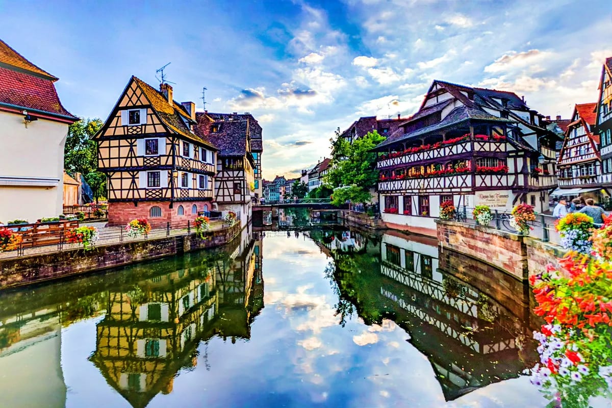 Best of Italy Switzerland and France Historic half-timbered buildings reflected in a canal in Strasbourg, France, with colorful flower baskets lining the waterway