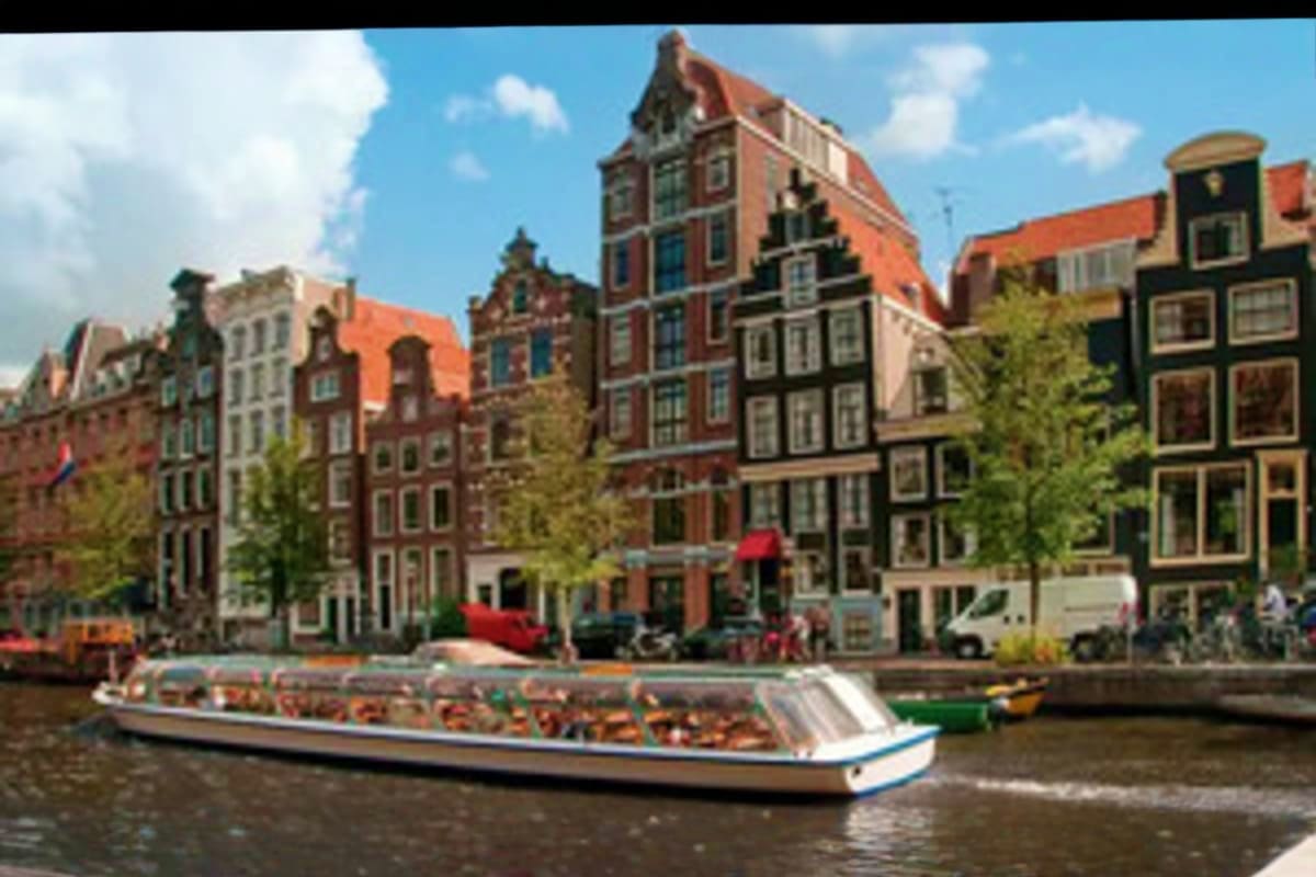 Tourist boat on Amsterdam canal with historic Dutch architecture and colorful gabled buildings lining the waterfront