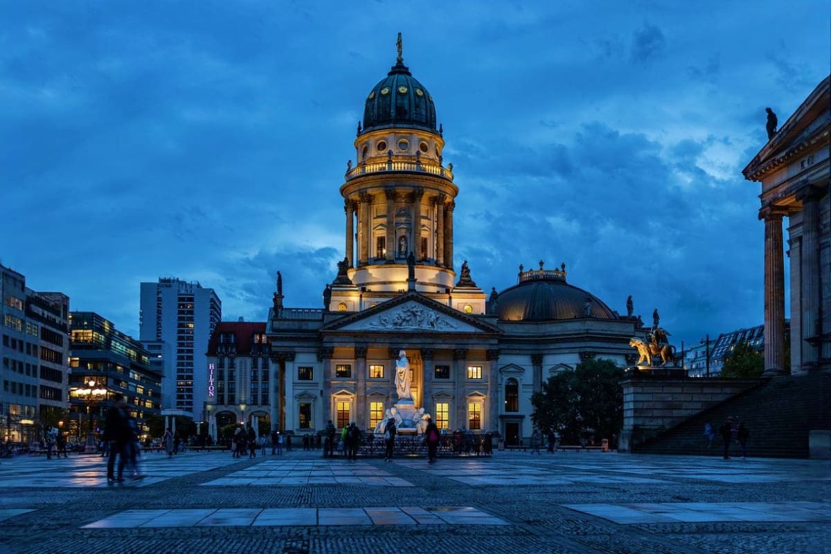 German Cathedral illuminated at dusk in Gendarmenmarkt square, Berlin, with tourists in plaza