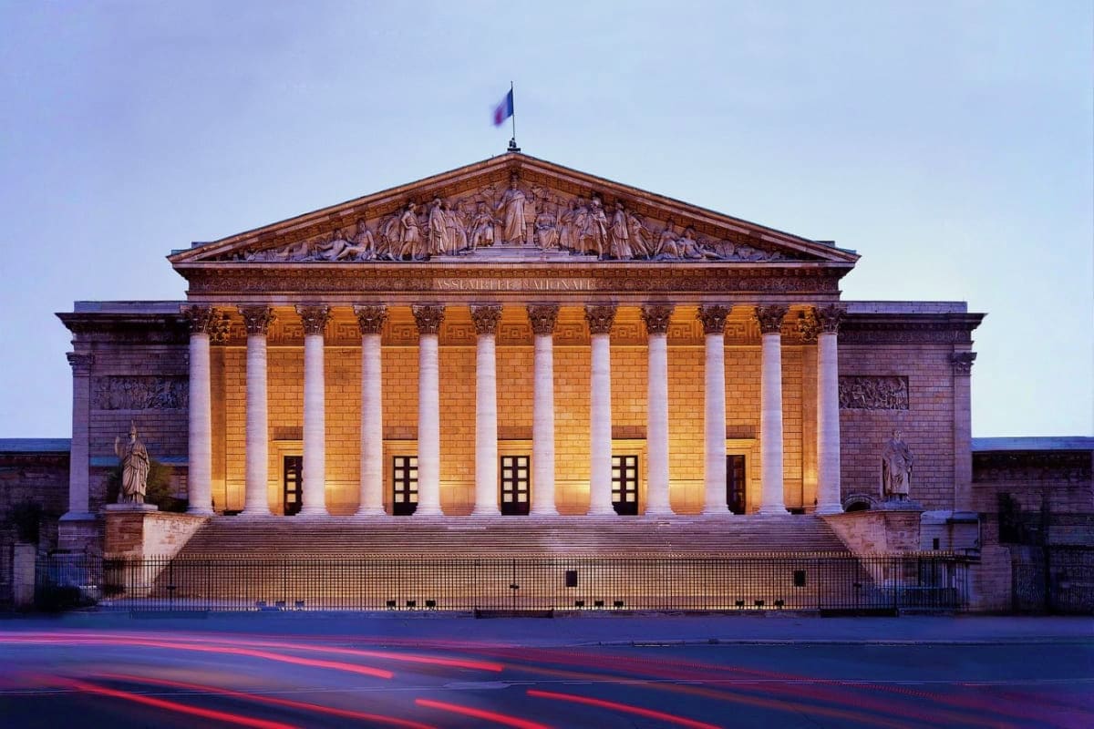 Palais Bourbon government building illuminated at dusk with classical columns and French flag in Paris