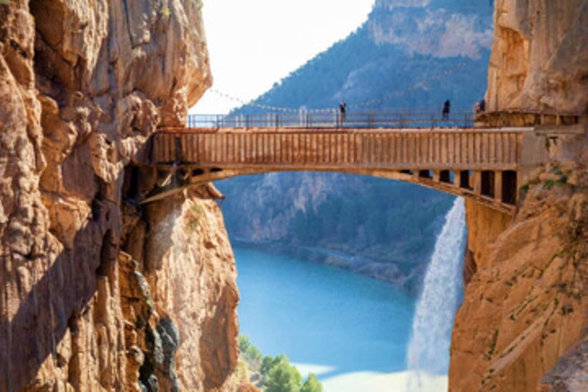 Wooden pedestrian bridge spanning between steep canyon walls above a turquoise lake surrounded by mountains