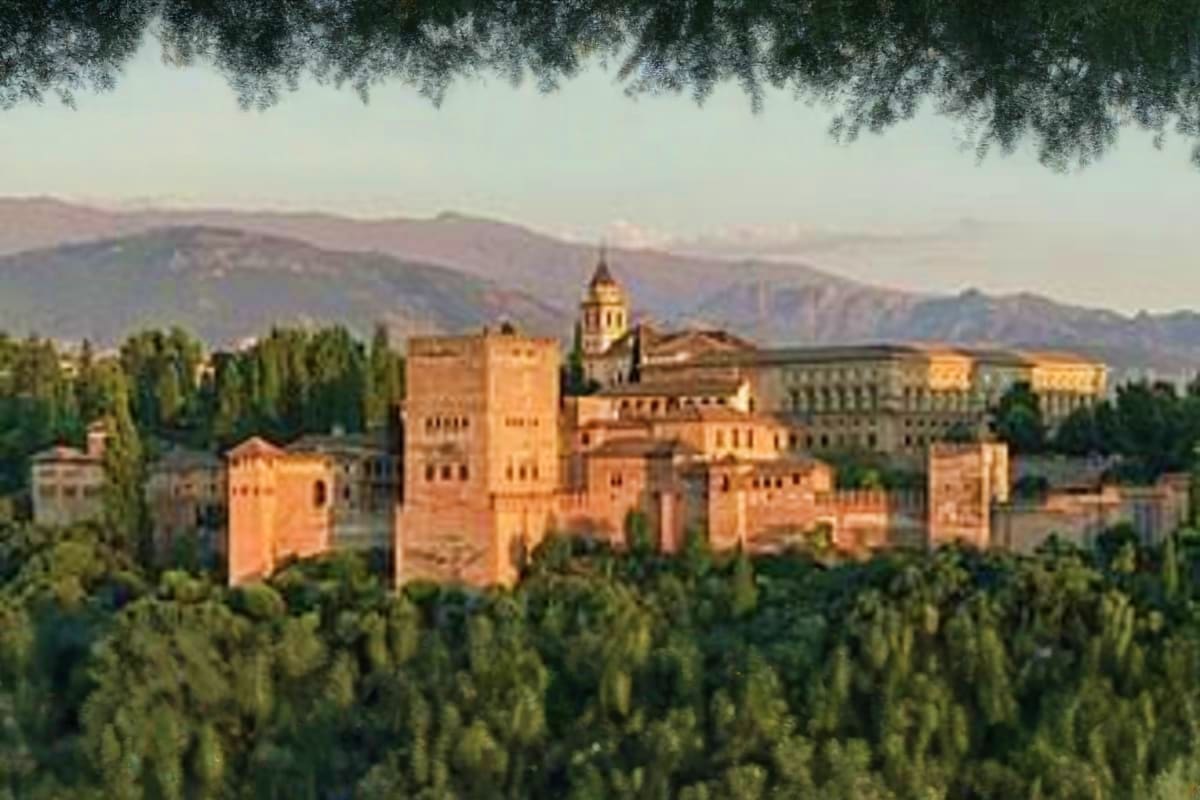 Alhambra palace in Granada Spain with golden stone buildings, tower, and surrounding cypress trees against mountain backdrop 