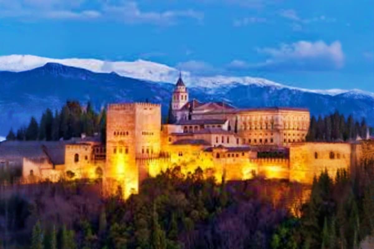 Alhambra palace illuminated at dusk with snow-capped Sierra Nevada mountains in background, Granada Spain