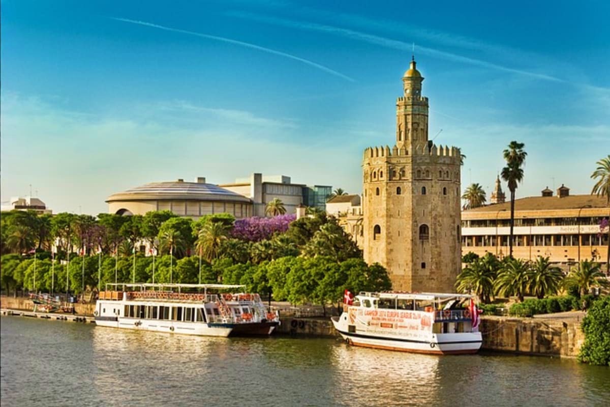 Seville riverfront with Torre del Oro tower, tour boats docked at the Guadalquivir River, palm trees and historic architectur