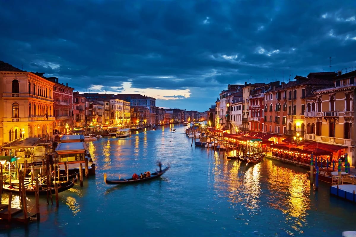 Venice Grand Canal at dusk with illuminated buildings, gondola, and boats reflecting in blue water