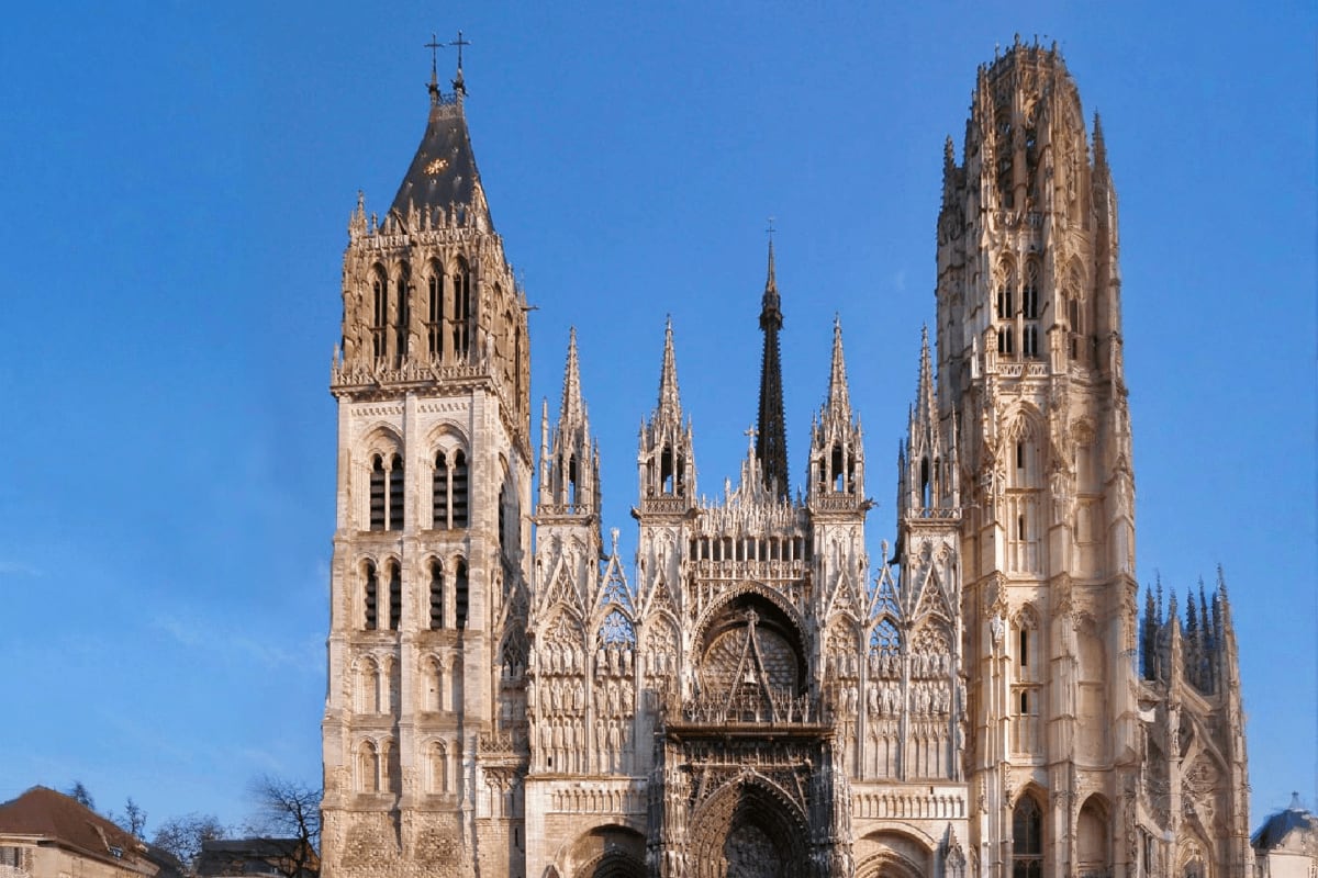 Rouen Cathedral's Gothic front facade with ornate twin towers and intricate stone carvings against a clear blue sky