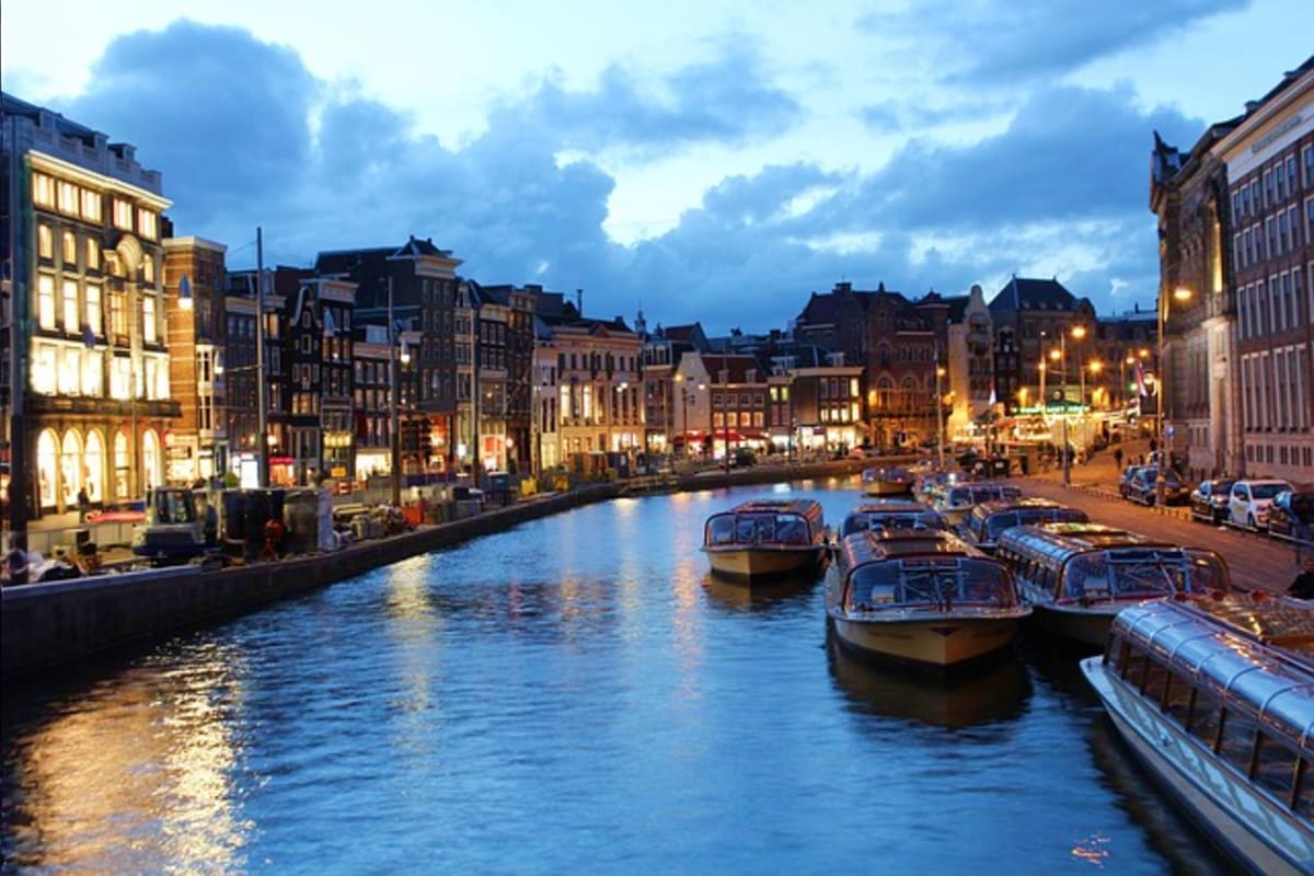 Historic Amsterdam canal at twilight with illuminated buildings, boats, and traditional architecture along the waterfront