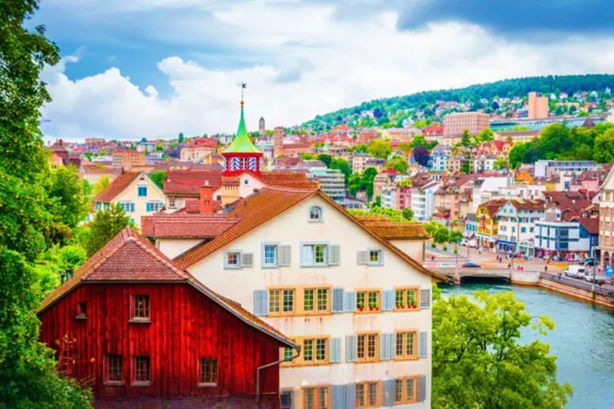 Historic riverside buildings with red and white architecture and green church spire in Zurich, Switzerland