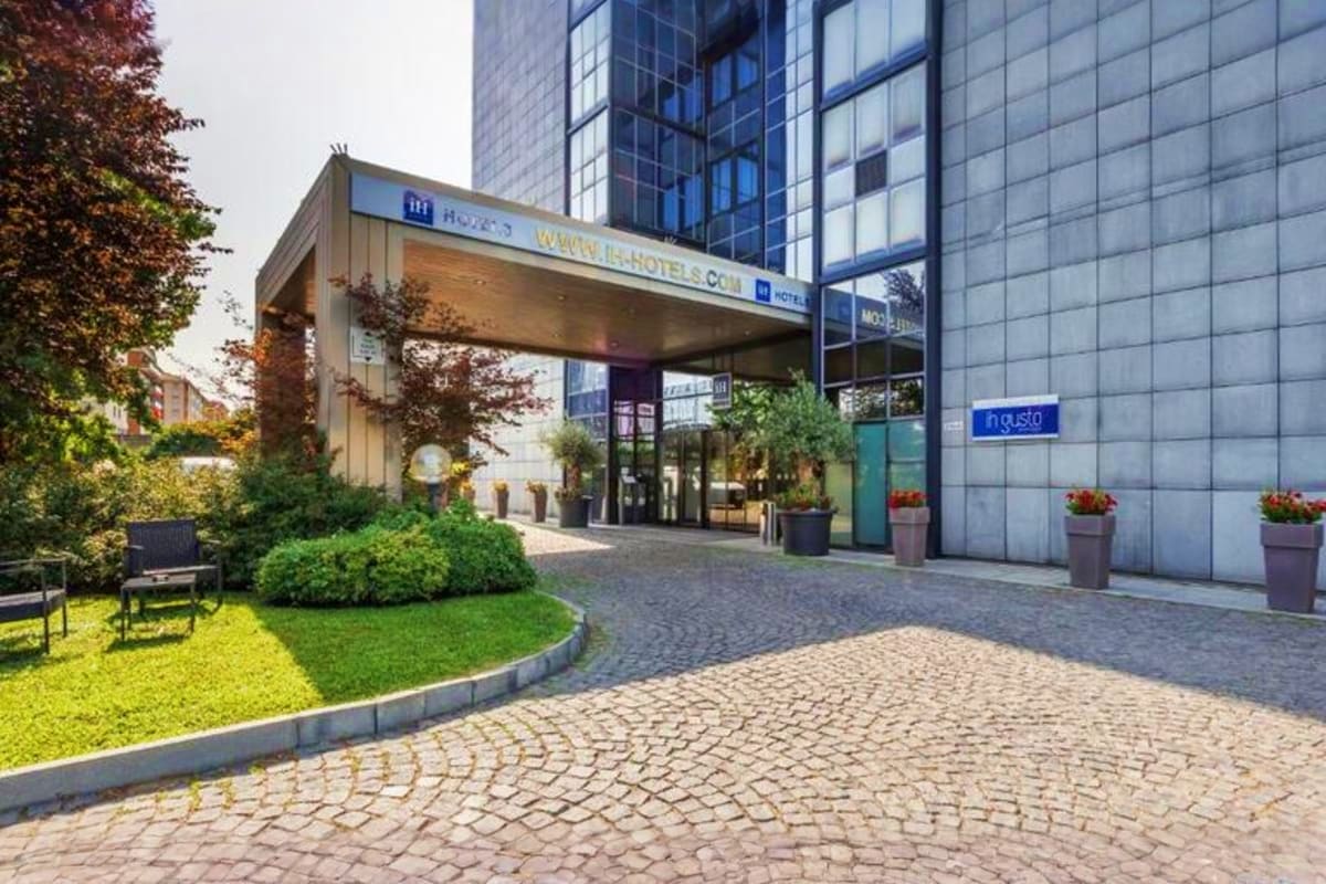 Modern hotel entrance with glass facade, green courtyard garden, and paved plaza in European city setting