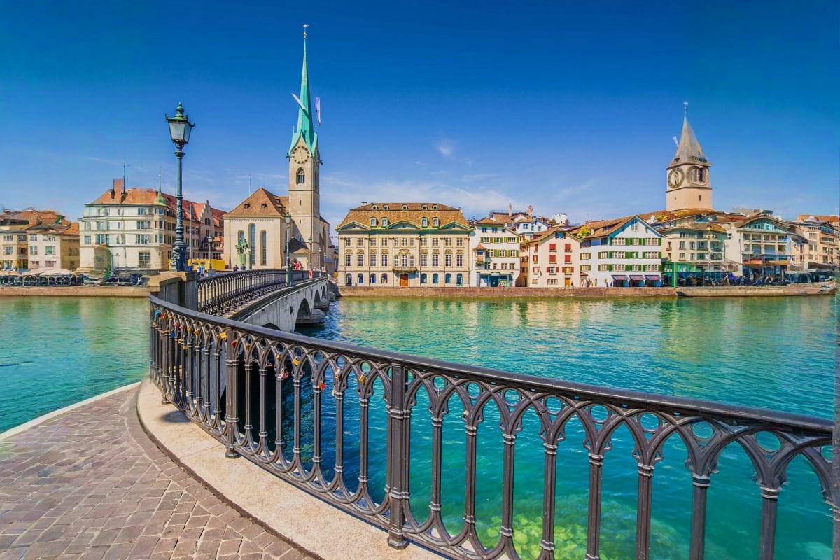 Western Europe Highlights Zurich waterfront with ornate black railing, historic churches with spires, and colorful buildings along turquoise river unde