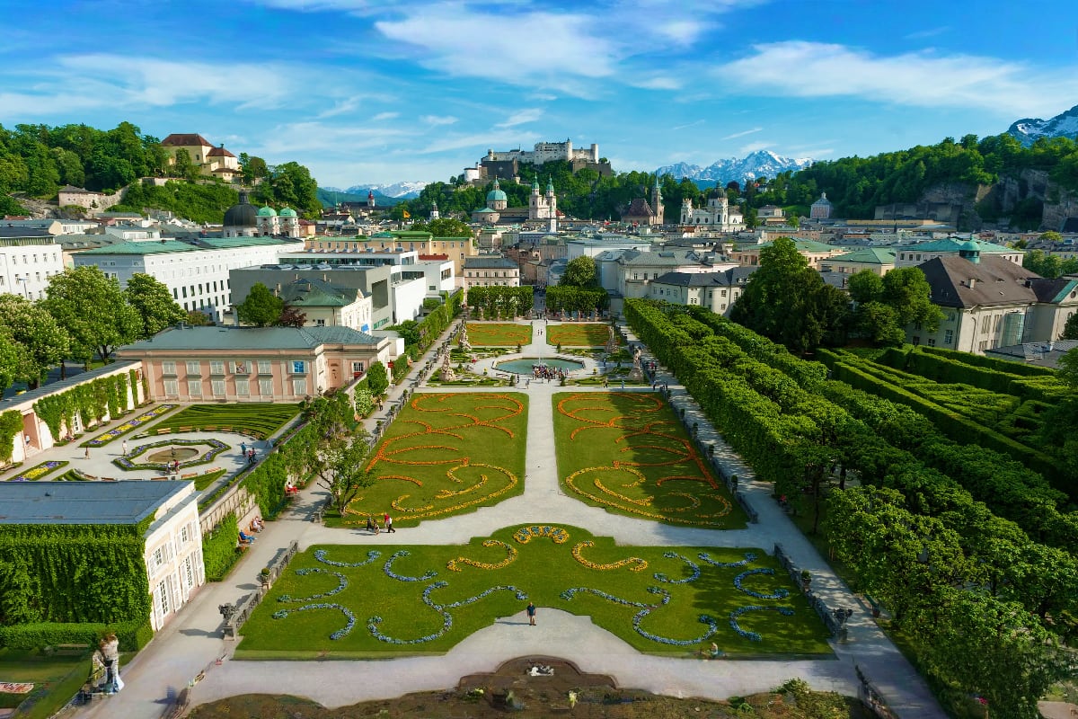 Italy to Amsterdam Tour Aerial view of Mirabell Gardens in Salzburg, Austria with formal hedges, flower beds, historic palace, and Alpine mountains i