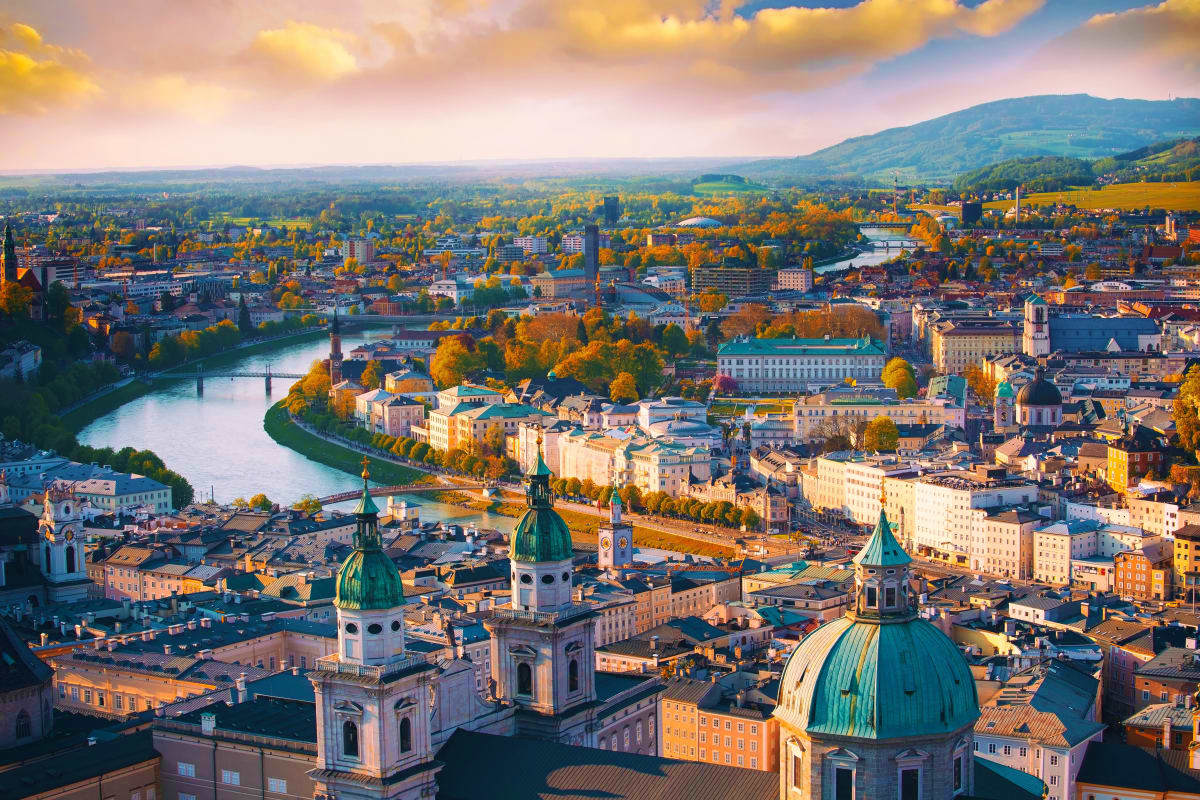 Aerial view of Salzburg's cathedral and Inn River with autumn foliage and Alpine mountains in background