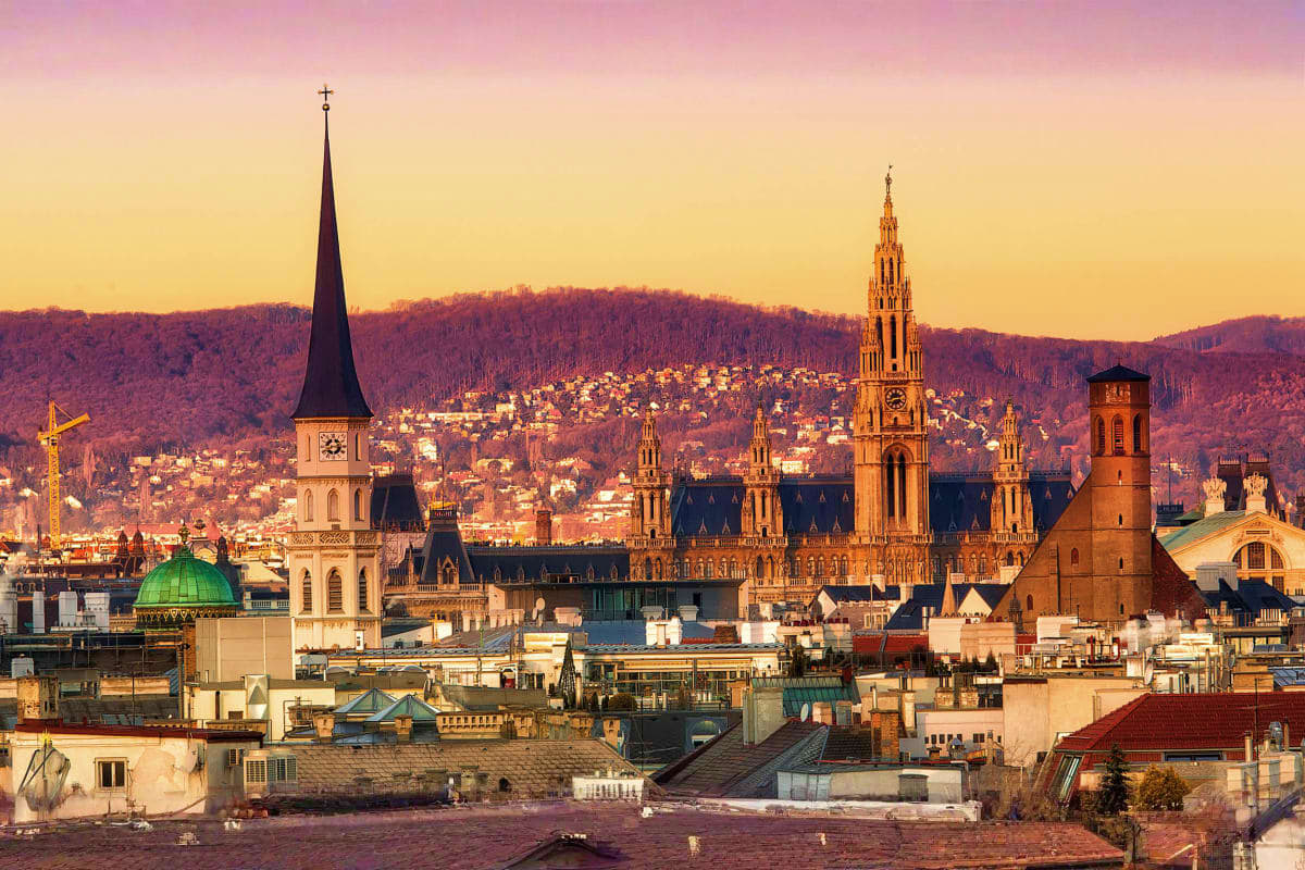 Vienna skyline at sunset with Gothic church spires, green dome, and forested hills in background
