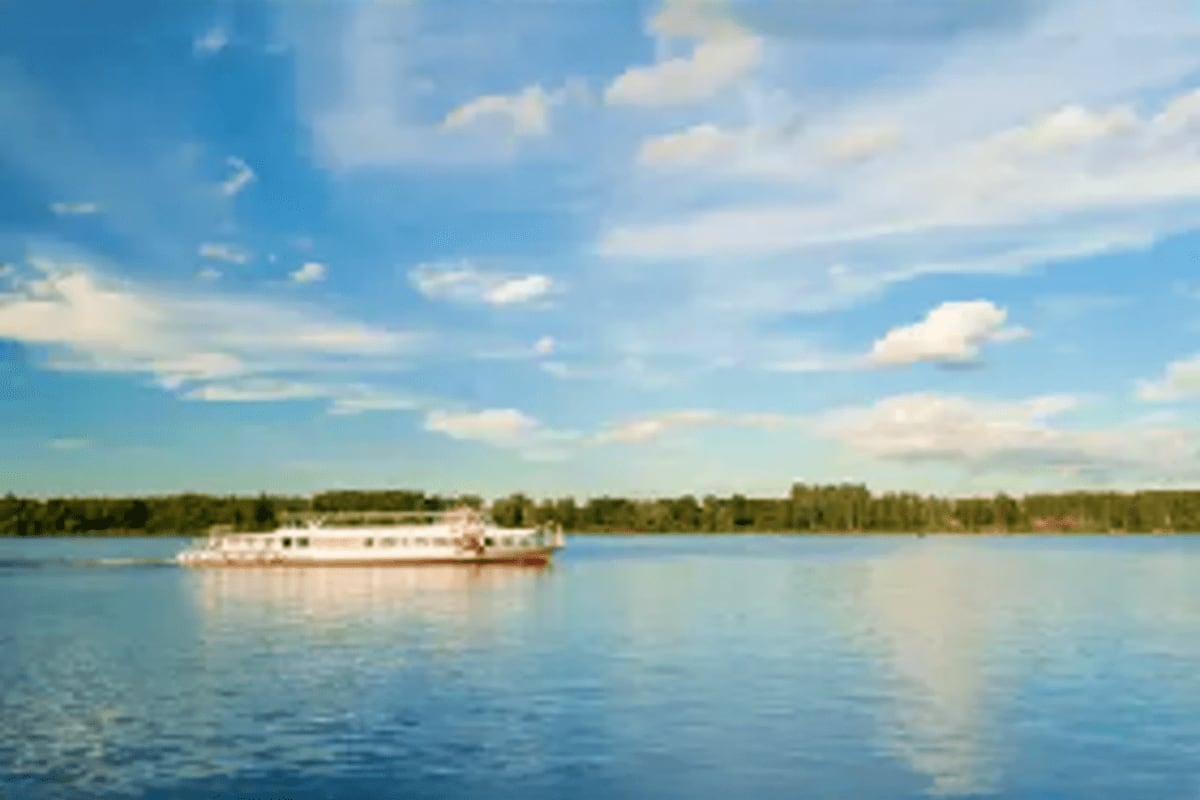 White river cruise ship sailing through calm blue water with forested banks and blue sky with white clouds